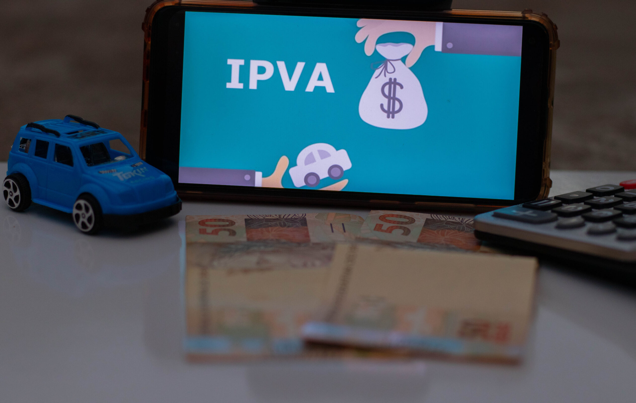 Um celular com uma imagem ao fundo escrito 'IPVA'