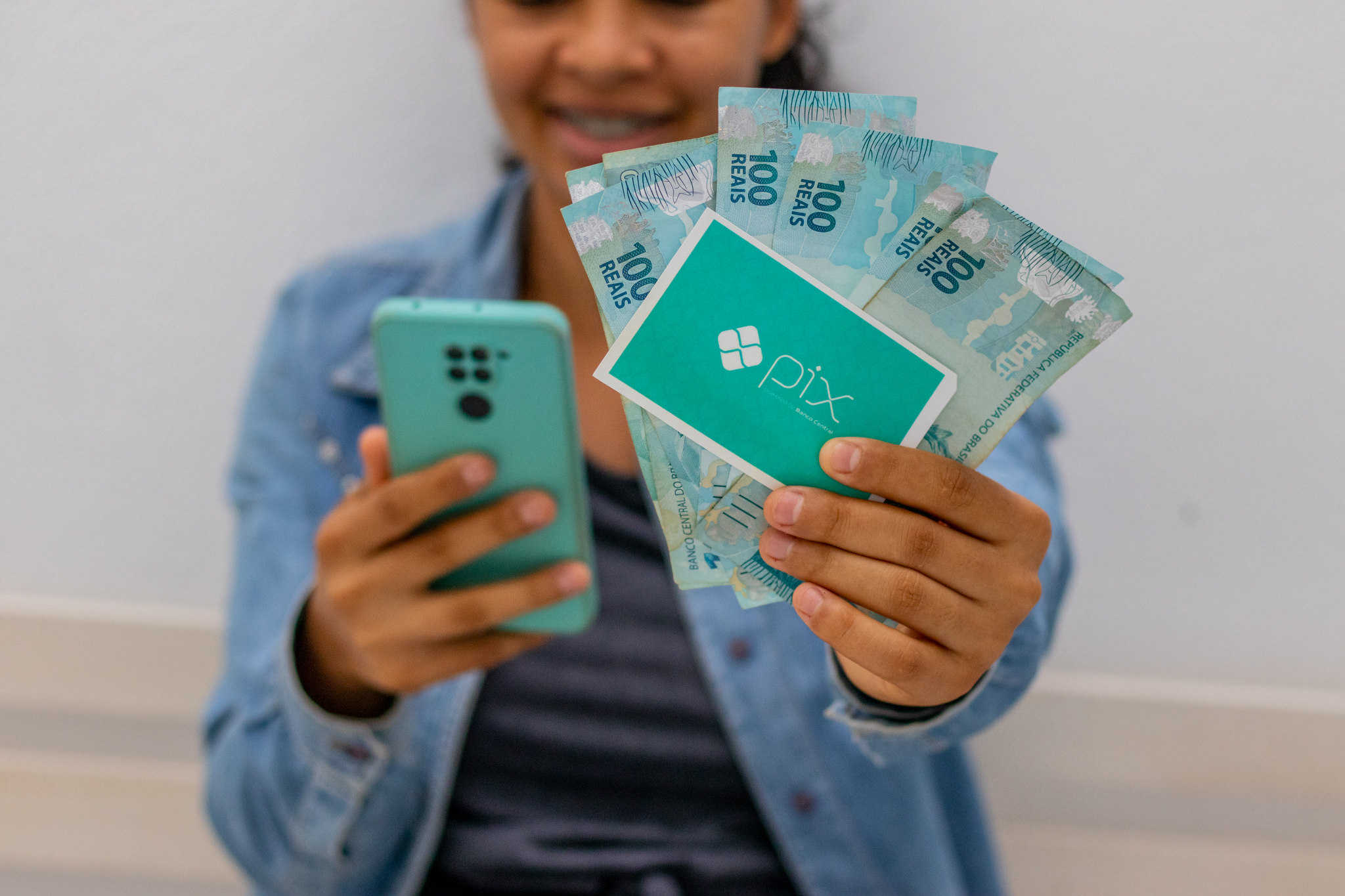 Pessoa segurando um celular e cédulas de dinheiro brasileiro