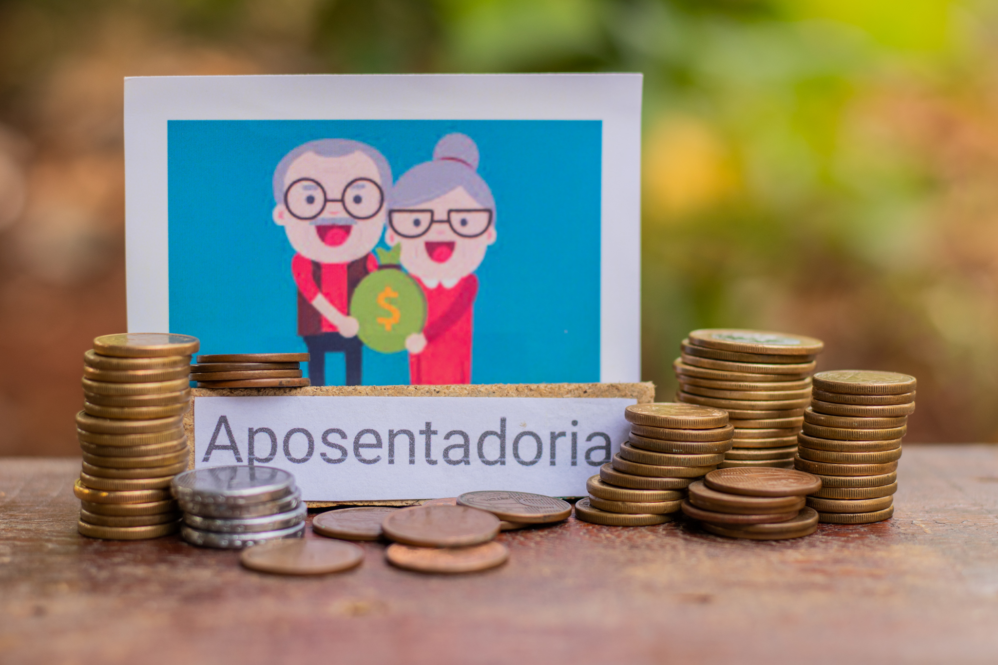Moedas de dinheiro brasileiro, um casal de idosos e o nome 'aposentadoria'