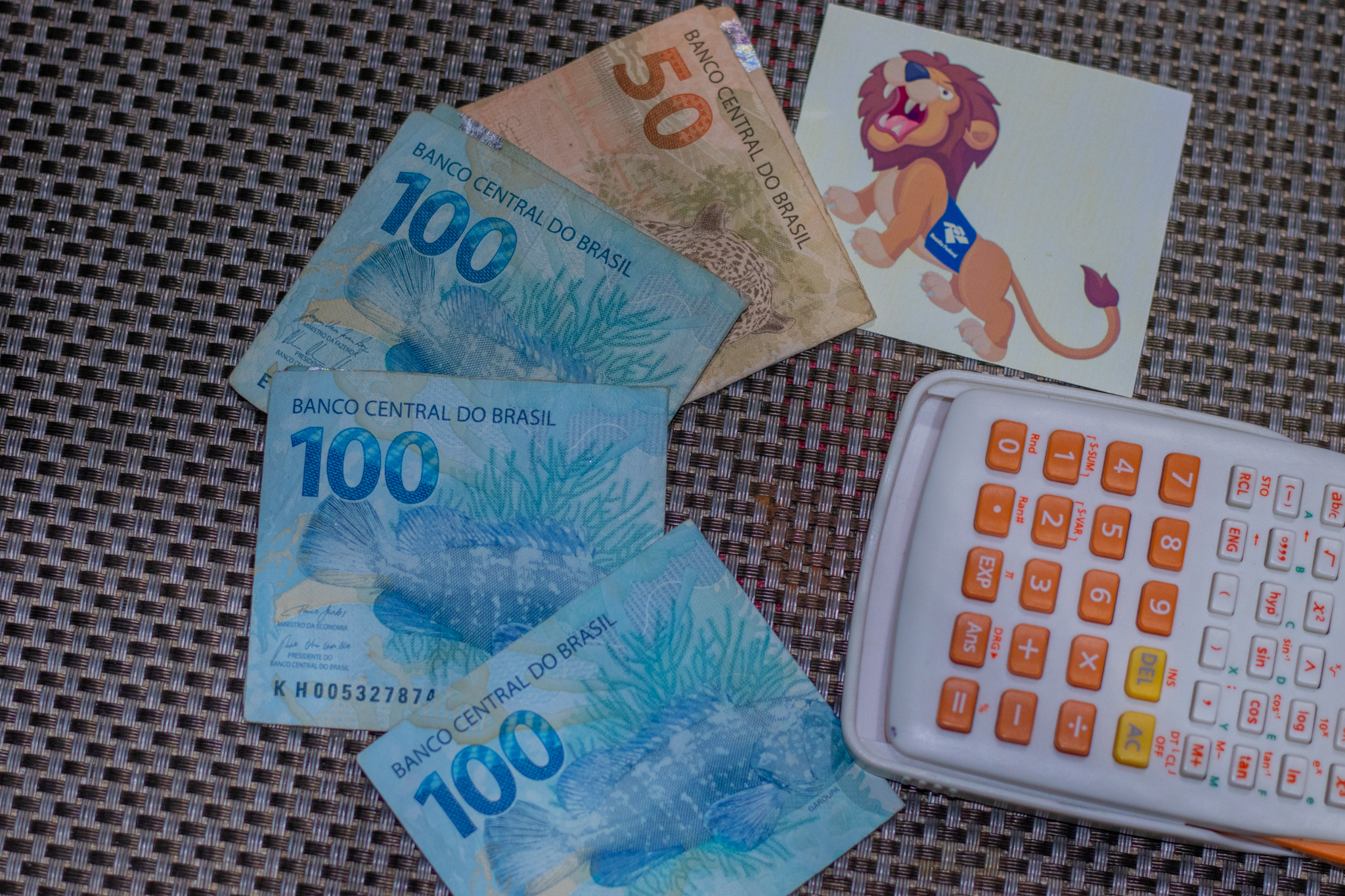 Cédulas de dinheiro brasileiro, uma calculadora e uma imagem de um leão