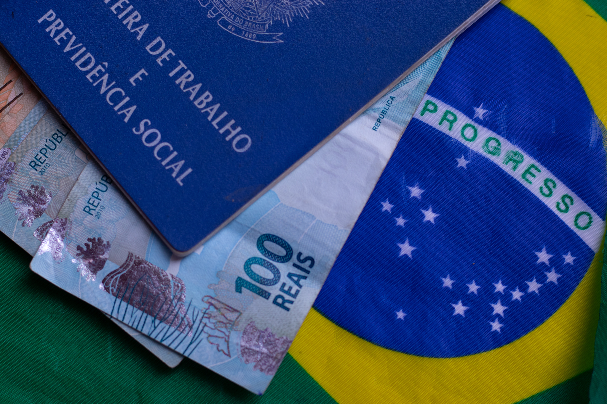 Carteira de trabalho, cédulas de dinheiro brasileiro e uma bandeira do Brasil