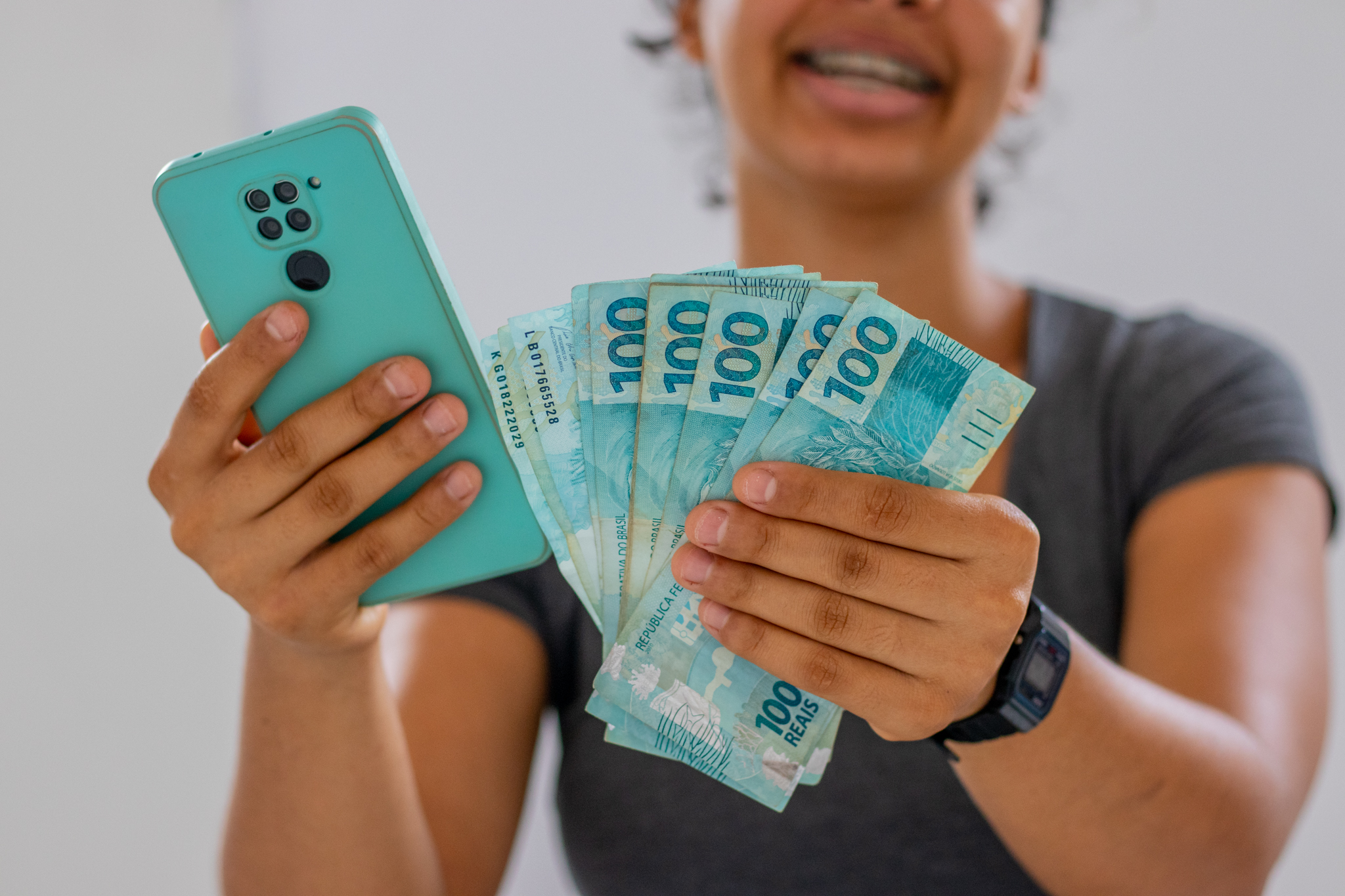 Mulher segurando dinheiro brasileiro e um celular
