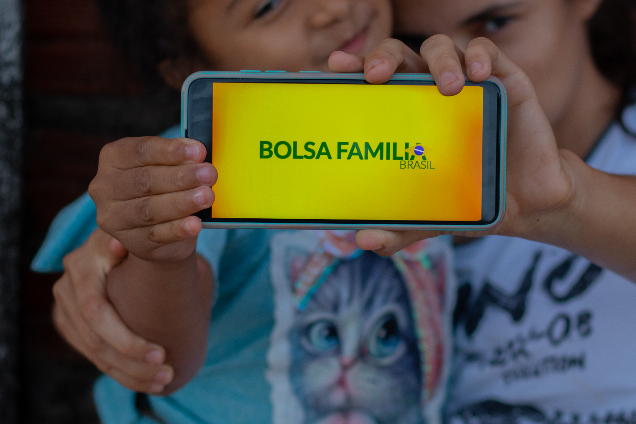 Uma mãe e sua filha segurando o celular com o nome Bolsa Família