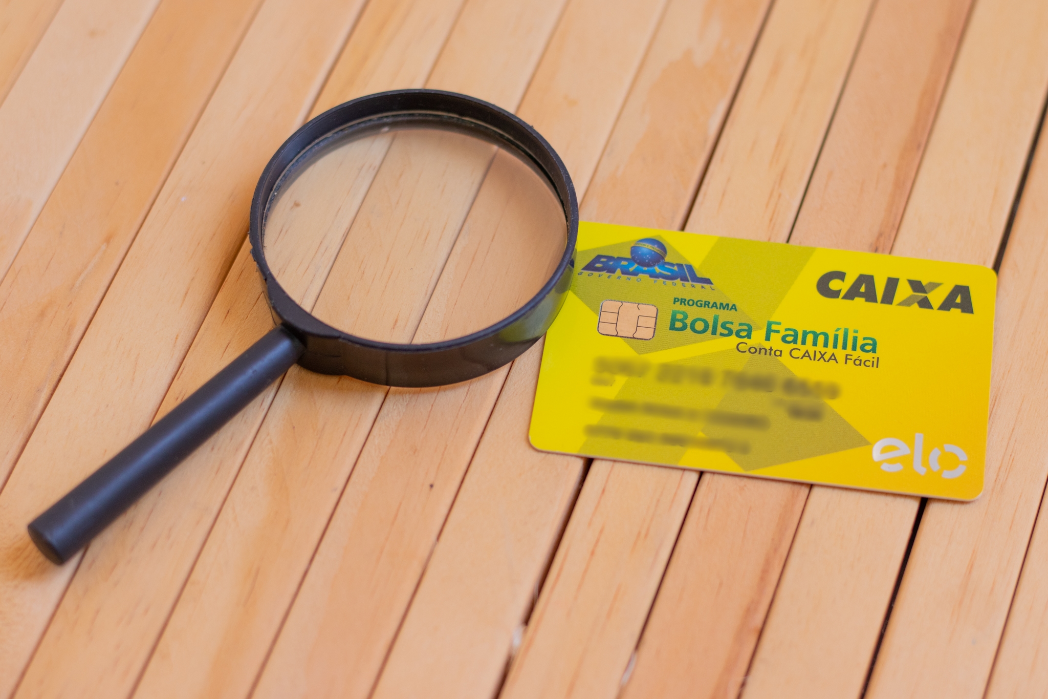 Uma Lupa e ao lado, o cartão do Bolsa Família