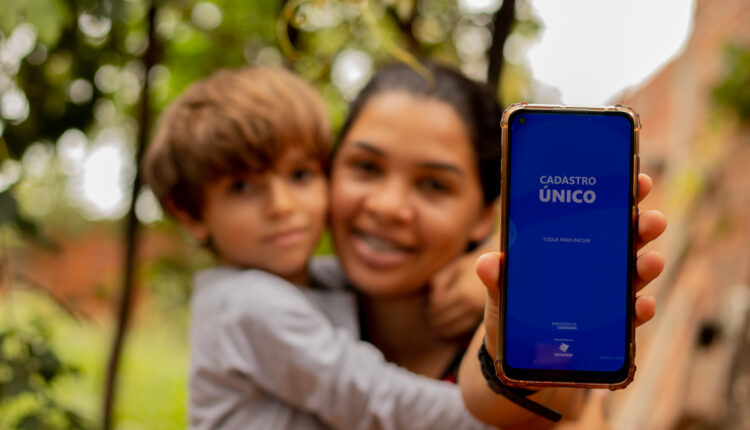 Mulher segurando celular com o aplicativo do CadÚnico aberto