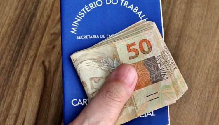Pessoa segurando Carteira de Tabalho, com notas de dinheiro em cima.