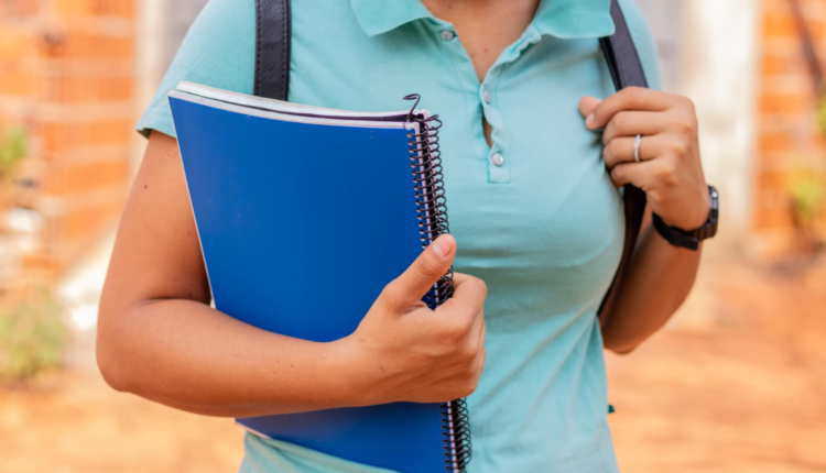 Foto de estudante segurando um carderno, com mochila.