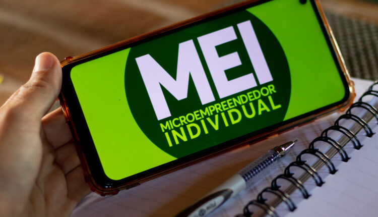 Pessoa segurando celular na horizontal, com logo do MEI.