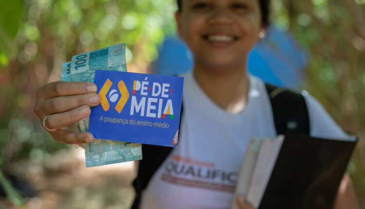 Criança mostrando notas de dinheiro e papel com logo do Pé de Meia para a câmera.