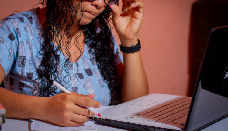 Mulher estudando para concurso, com notebook e papel a frente.
