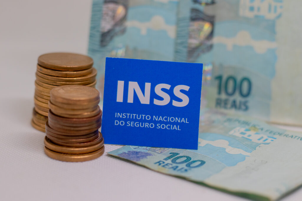 Notas e moedas ao lado de placa do INSS.