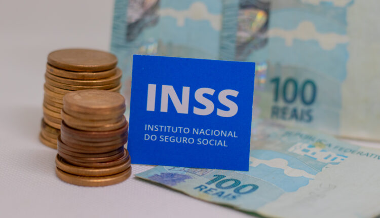 Notas e moedas ao lado de placa do INSS.