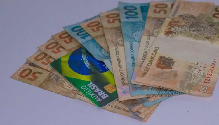 Notas de 100 e 50, com cartão do Auxílio Brasil.