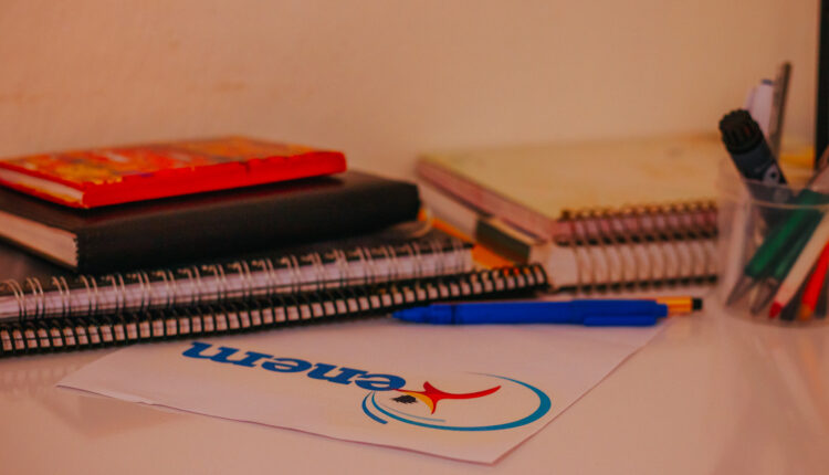 Mesa de estudos com cadernos e papel em evidência com logo do Enem.