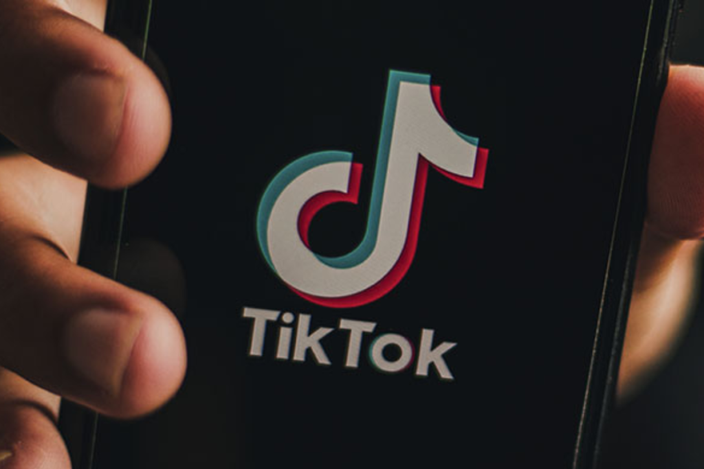 Mão mostrando tela de telefone, com logo do Tik Tok.