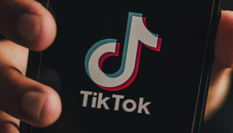 Mão mostrando tela de telefone, com logo do Tik Tok.