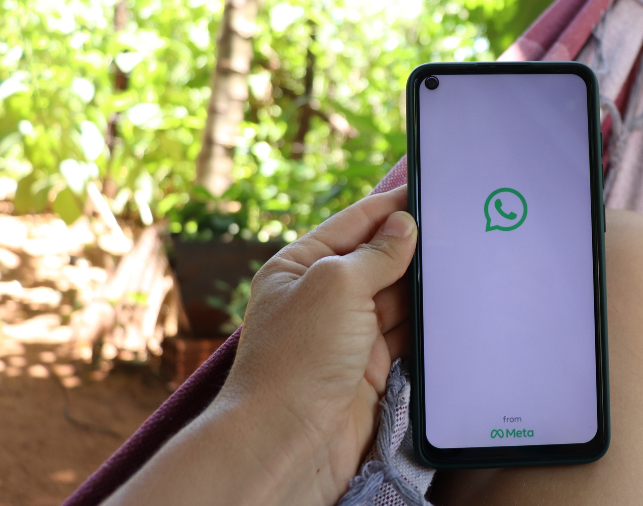 Mão segundo celular com logo do WhatsApp na tela.