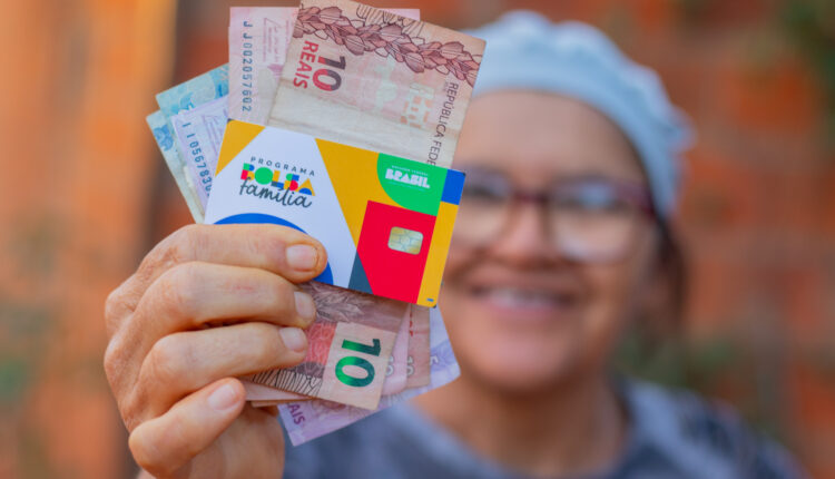 Mulher segurando notas de dinheiro e cartão do Bolsa Família.