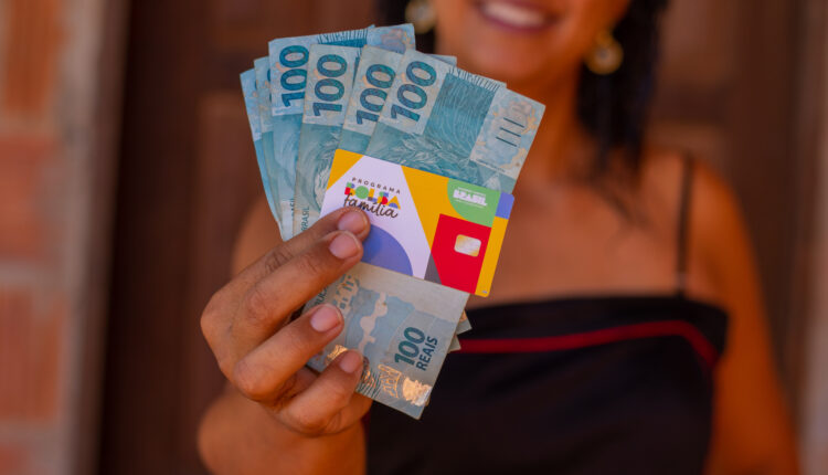 Pessoa segurando cartão do Bolsa Família e notas.