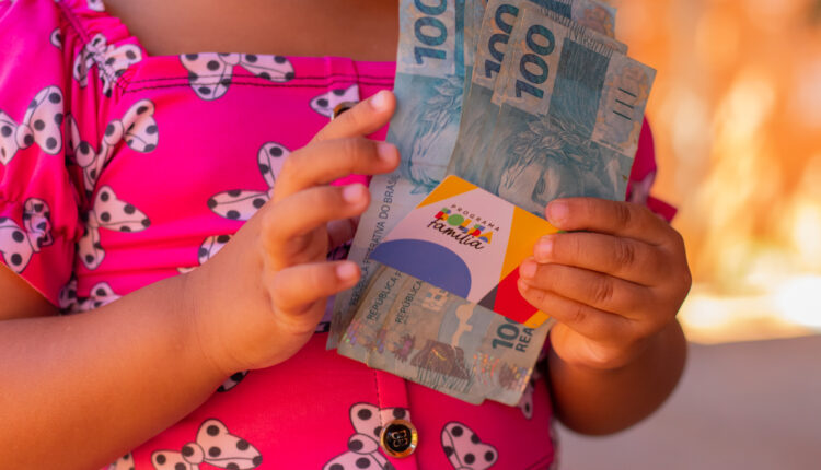 Pessoa segurando notas de dinheiro e cartão do Bolsa Família.
