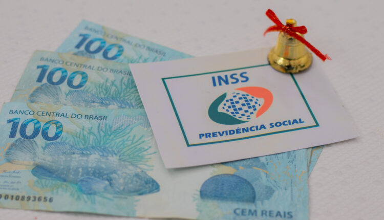 Notas de dinheiro em mesa, com logo do INSS ao lado.