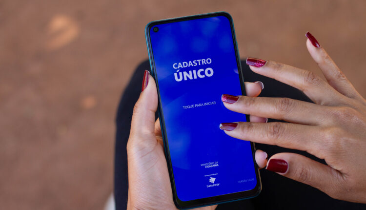 Mulher segurando celular aberto no app CadÚnico.
