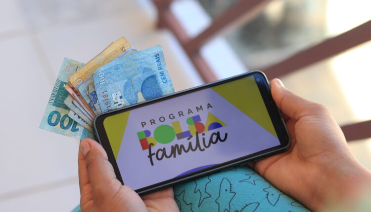 Pessoas segurando notas de dinheiro e celular.
