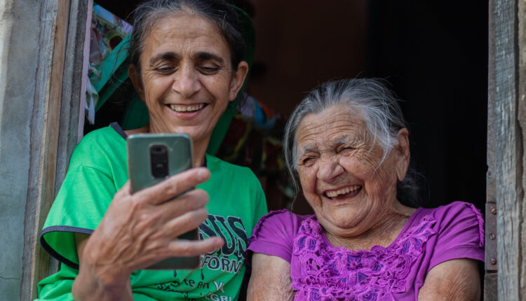 Duas idosas rindo olhando para o celular.