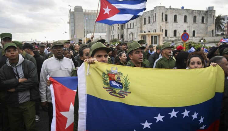 Membros das Forças Armadas seguram bandeiras venezuelanas e cubanas durante um protesto “anti‑imperialista” em frente à Embaixada dos EUA contra a incursão dos EUA na Venezuela, onde 32 soldados cubanos perderam a vida, em Havana, em 16 de janeiro de 2026.