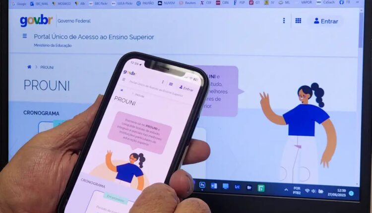Candidato com celular nas mãos em frente a um computador para fazer a inscrição no Prouni