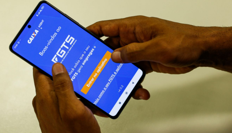 Mãos de uma pessoa negra segurando um celular. Na tela do dispositivo está o aplicativo do FGTS, o meio no qual moradores de Morretes podem solicitar o Saque Calamidade do FGTS.